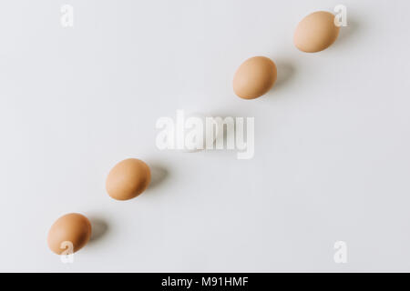 Weiße und braune Eier in einer Reihe auf weißem Hintergrund Stockfoto