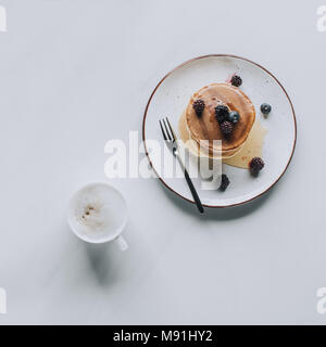 Blick von oben auf die leckere gesunde Pfannkuchen und Tasse Cappuccino auf Grau Stockfoto