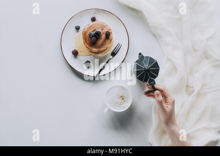Blick von oben auf die Person, die Kaffeemaschine beim essen Pfannkuchen mit Beeren für das Frühstück Stockfoto