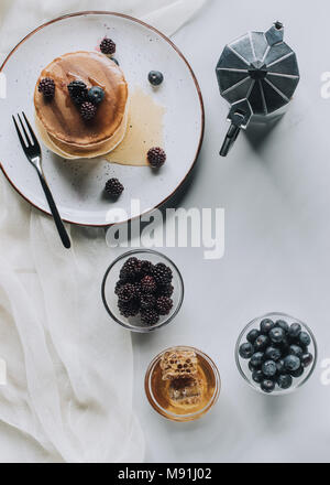 Draufsicht auf das leckere Frühstück mit Pfannkuchen, Beeren, Honig und Kaffee auf Grau Stockfoto