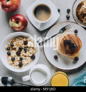 Blick von oben auf die lecker gesundes Frühstück mit Pfannkuchen, Obst und Müsli auf Grau Stockfoto