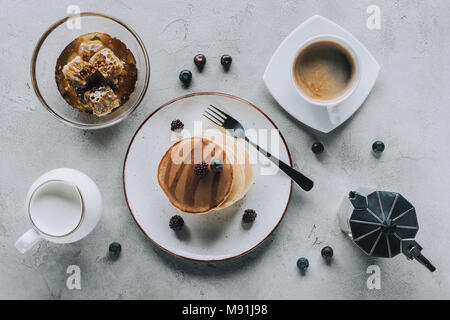 Blick von oben auf die süß lecker Pfannkuchen mit Kaffee, Milch, frische Beeren und Honig auf Grau Stockfoto