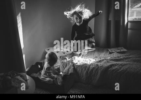 Mädchen springt auf Bett im Sonnenschein Stockfoto