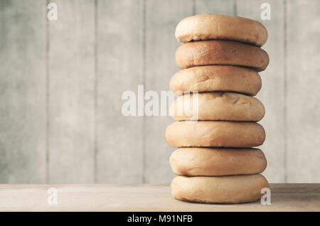 Ein grosser Stapel von ganzen Bagels, auf hellem Holz Schneidbrett mit Beplankten Hintergrund. Neutrale Farbtöne mit Filter Effekte angewendet. Stockfoto