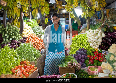 Eine junge Frau aus Sri Lanka Händler an ihrem bunten lebendigen in der Zentrale Markt von Nuwara Eliya Verkauf von frischem Obst und Gemüse aus eigenem Anbau. Stockfoto