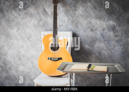 Notebook mit Bleistift zum Komponieren von Musik auf Tabelle mit klassischer Gitarre an der Wand Stockfoto