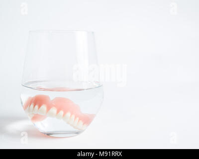 Ein acryl Zahnersatz in einem Glas Wasser auf weißem Hintergrund eingetaucht Stockfoto