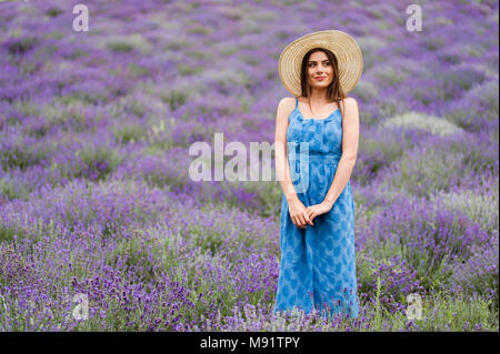 Die Frau in der Mitte von einem Lavendelfeld, trägt einen eleganten blauen Kleid und einen Strohhut. Stockfoto