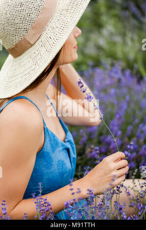 In der Nähe der schöne junge Frau, die in einem Feld von Lavendel trägt einen blauen vintage Kleid und einen Strohhut. Stockfoto