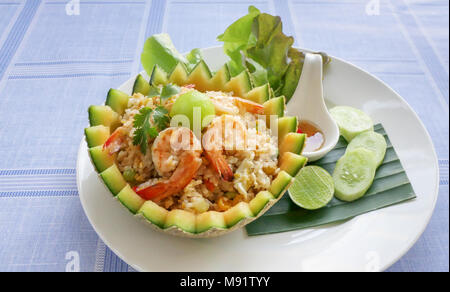 Gebratener Reis mit Garnelen in der Melone Schale mit frischen Gurken, Salat, Kalk und würzige Fischsauce serviert. Stockfoto