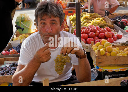 Ein Mann Verkauf von frischen Produkten aus Kisten in der Dezerters" Basar Open-Air-Markt Trauben essen aus seinem Display, Tiflis, Georgien Stockfoto