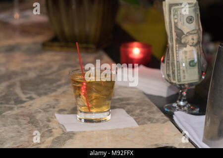 Whiskey oder Scotch on the rocks Trinken sitzen auf einem Restaurant bar Zähler nach oben. US Dollar Bill cash Tipps sitzen aus Glas für guten Service Stockfoto