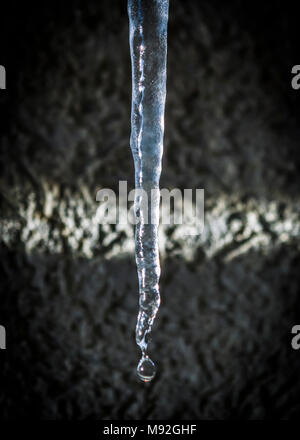 Schmelzenden Eiszapfen an der sonnigen Morgen. Große schmelzenden Eiszapfen auf einem Hausdach, verschmierte Wand im Hintergrund. Stockfoto