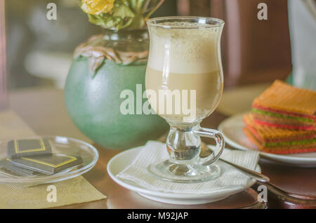 Kaffee raf in einem Glas mug. Latte Macchiato mit Schaum auf Hintergrund mit Blumen, Kuchen und Vintage verzierende Elemente Stockfoto