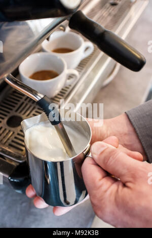 Barista dämpfen und Aufschäumen der Milch in Edelstahl Zuhaltung mit Espresso maching für Cappuccino oder Latte Stockfoto