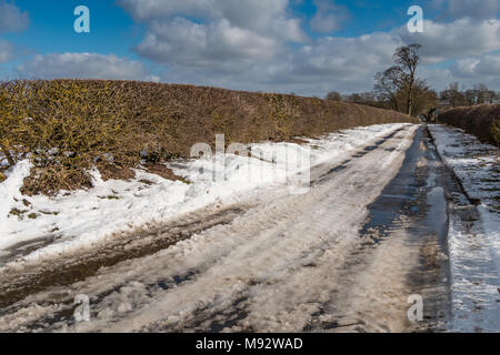Eine ländliche Land Strasse mit Schnee und Eis auftauen im hellen Sonnenschein nach Blizzard Bedingungen zwei Tage zuvor. Stockfoto