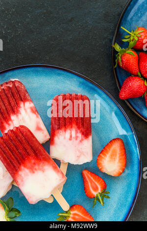 Hausgemachte Vegan Erdbeere Popsicle mit Erdbeersaft und Kokosmilch auf dunklem Marmor Hintergrund. Sommer essen Konzept. Ansicht von oben. Stockfoto