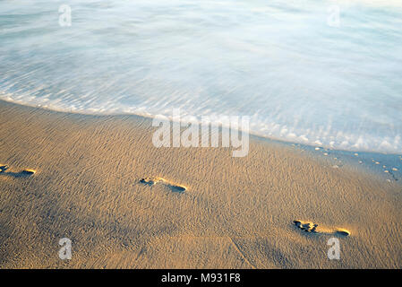 Fußabdrücke auf einen Strand mit Wellen am Ufer. Stockfoto