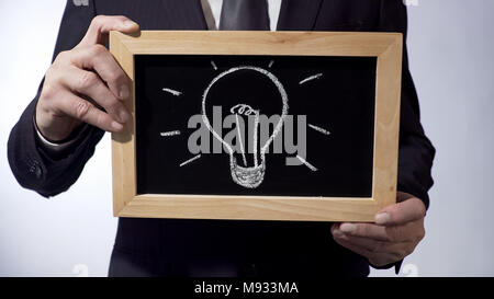 Glühlampe Zeichnung auf Tafel, Mann im schwarzen Anzug Holding unterzeichnen, Geschäftsidee Stockfoto