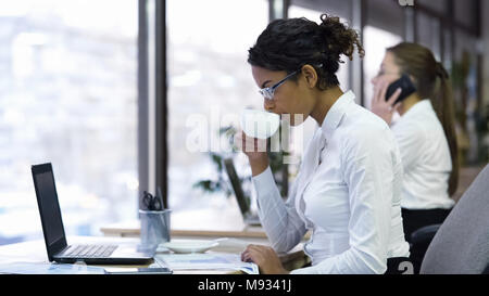 Attraktive weibliche Büroangestellte trinken Kaffee und Lesen der Diagramme Stockfoto