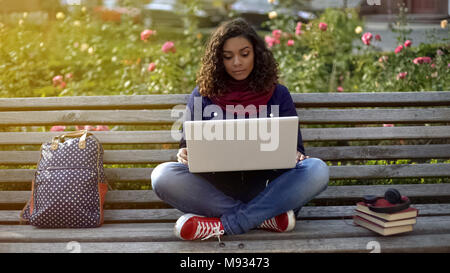 Ernsthafte Schülerin mit Freunden zu reden über Laptop Kamera, sitzt auf der Bank Stockfoto