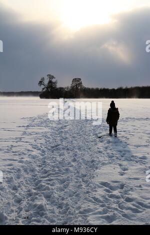 Eine kleine Abbildung auf einem schneebedeckten Weg über Felder Silhouette Stockfoto