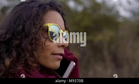 Nachdenklich gemischten Rasse Frau in gelb Sonnenbrille sprechen auf dem Smartphone, close-up Stockfoto