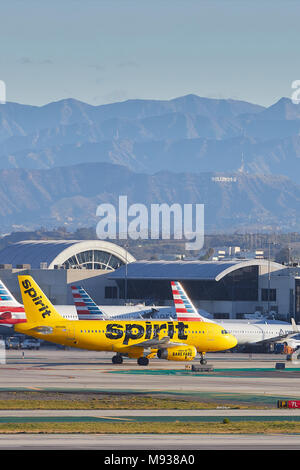 Spirit Airlines A319, In leuchtend gelben Anstrich, das Rollen an die Passagierterminals am internationalen Flughafen von Los Angeles, LAX, das Hollywood Zeichen hinter sich. Stockfoto