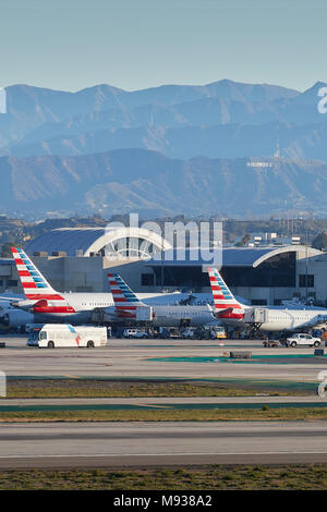 Heckflossen der geparkten American Airlines Flugzeuge am Flughafen LAX, Los Angeles International Airport mit Der Hollywood Sign und die San Gabriel Berge dahinter. Stockfoto