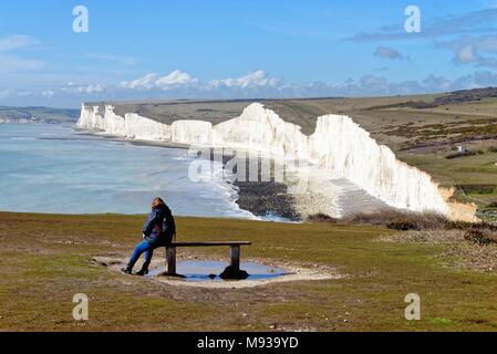 Frau sitzt auf der Klippe Sitzbank bei Blick auf die Sieben Schwestern Kreidefelsen am Birling Gap in den South Downs National Park East Sussex England suchen Stockfoto