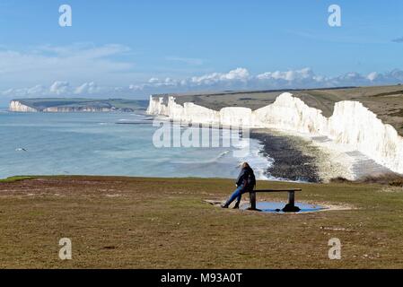 Frau sitzt auf der Klippe Sitzbank bei Blick auf die Sieben Schwestern Kreidefelsen am Birling Gap in den South Downs National Park East Sussex England suchen Stockfoto