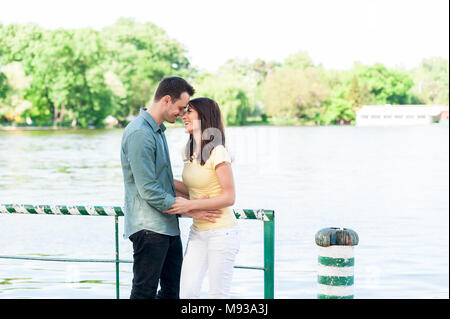 Fröhliche und spontane Paar in Liebe, halten sich an den Händen auf einem steinernen Pier auf einem natürlichen See Spaß, küssen, umarmen und Lachen im Freien. Stockfoto