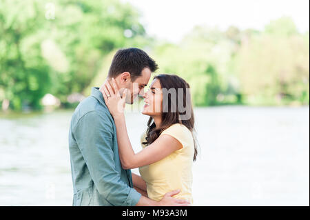 Fröhliche und spontane Paar in Liebe, halten sich an den Händen auf einem steinernen Pier auf einem natürlichen See Spaß, küssen, umarmen und Lachen im Freien. Stockfoto