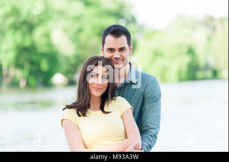 Fröhliche und spontane Paar in Liebe, halten sich an den Händen auf einem steinernen Pier auf einem natürlichen See Spaß, küssen, umarmen und Lachen im Freien. Stockfoto