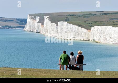 Drei Personen sitzen auf einer Klippe Sitzbank bei der Ansicht der Sieben Schwestern Kreidefelsen suchen, Birling Gap East Sussex England Großbritannien Stockfoto