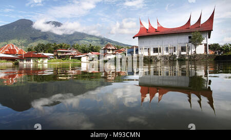 Landschaft von Sumatra. Atemberaubende Aussicht auf Mount Merapi aus über einen See mit Minangkabau haus dach Stil im Wasser spiegelt. Symmetrische Spiegelbild Stockfoto