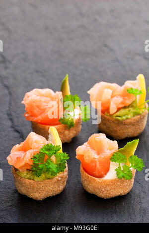 Croustades knuspriges Gebäck Fälle mit gesalzenen Lachs und Avocado auf schwarzen Stein Hintergrund Stockfoto