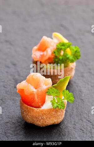 Croustades knuspriges Gebäck Fälle mit gesalzenen Lachs und Avocado auf schwarzen Stein Hintergrund Stockfoto