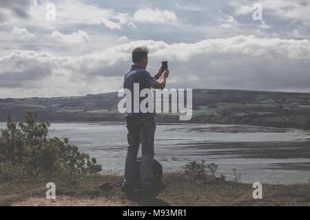 Mann, der ein Handy-Foto von der Ansicht auf dem Cleveland Weg in der Nähe von Robin Hoods Bay in North Yorkshire Stockfoto