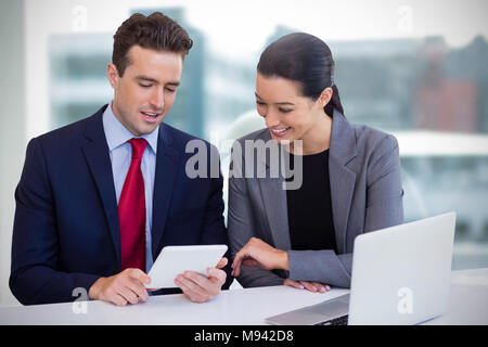 Das zusammengesetzte Bild von Führungskräften diskutieren über Tablet während vor weißem Hintergrund sitzen Stockfoto