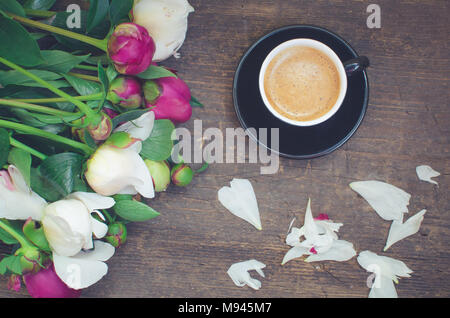 Kaffeepause. Kaffee und Blumen Pfingstrosen. Eine Tasse Kaffee und Pfingstrosen auf einem Holztisch. Frühstück am Muttertag, Valentinstag oder Tag der Frauen. Feder Stockfoto
