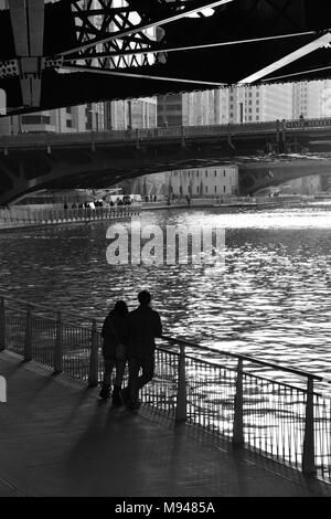 Ein paar wird von der späten Nachmittagssonne Silhouette beim Stehen auf dem Geländer auf der Chicago Downtown Riverwalk. Stockfoto