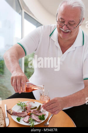 Fat man Essen viel ungesunde Nahrungsmittel viel Käse, Fleisch- und Wurstwaren trinken ein Glas Wein im Freien auf einem roten Ziegelmauer Stockfoto