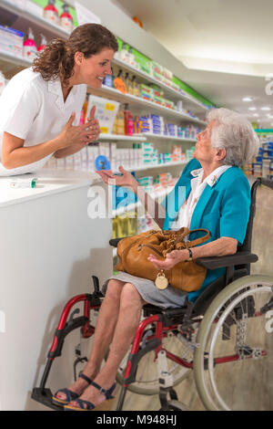 Weibliche Apotheker nehmen und erklären, Verordnung von behinderte Frau Rollstuhl in einem pharmafy Stockfoto