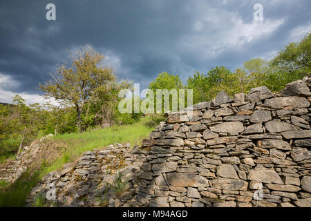 Alte Römische Mauer aus Stein, beleuchtet von der Sonne in Stürmisches Wetter, schwere Wolken und Grüner Baum im Frühling auf einem Weg in der Nähe von Kovachevitsa, Bulgarien Stockfoto