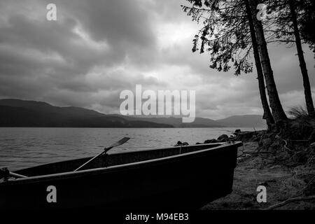 Kleines Fischerboot Silhouette am Ufer mit seitlichem Kiefern in trüben dunklen regnerischen Morgen am See Dospat, Rhodopen Gebirge, Bulgarien Stockfoto