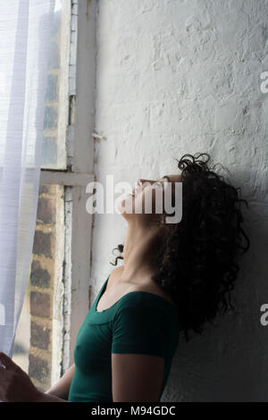 Seitenansicht eines betonte, junge Frau, die am Fenster Stockfoto