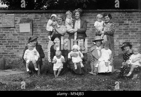 Mütter und Babys sammeln sich an einer gemeinschaftlichen Messe in England für ein Gruppenfoto, Ca. 1930. Stockfoto