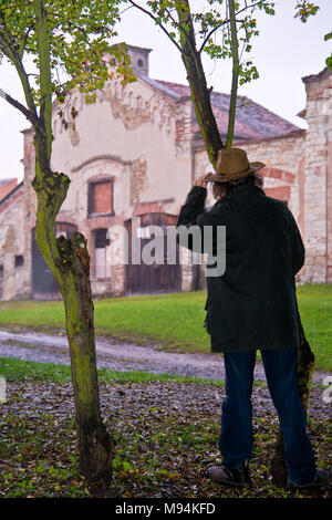 Cowboy bis hinter Bäumen und Beobachten der alten Farm Stockfoto