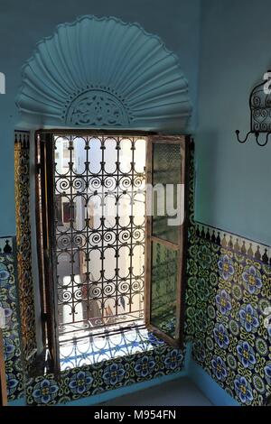 Ein Fenster wird durch zarte Metall ranken geschützt, innerhalb eines halben geflieste Zimmer mit fächerförmigen Dekoration in Marokko über Stockfoto